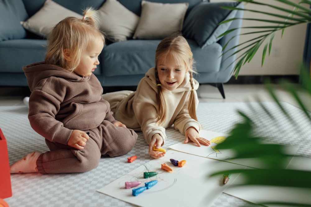 Dvoje dece se igraju na podu i crtaju u prostoru prilagođenom njihovom uzrastu